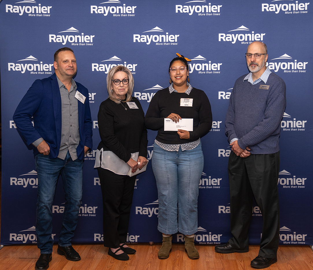 Four people standing together, one holding a check