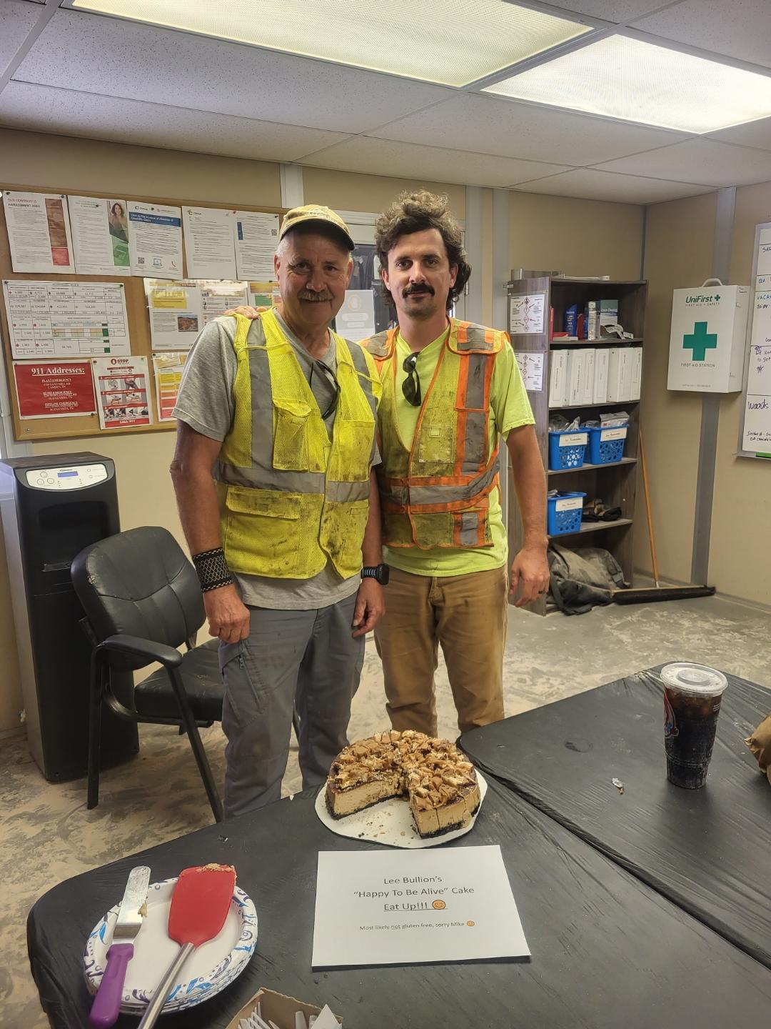 Two people in high-visibility vests standing together behind a table with a cake on it