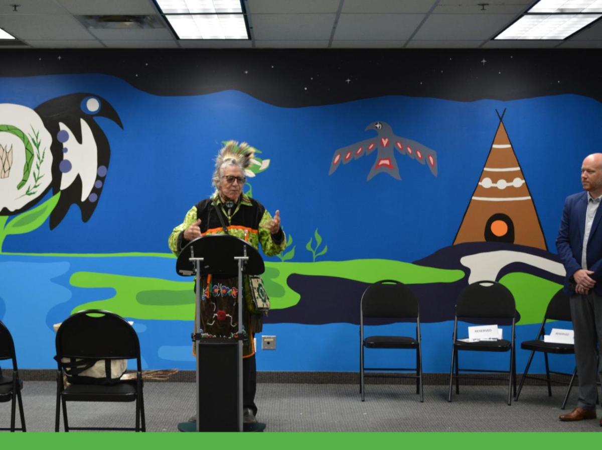 Someone speaking at a podium, with a large mural in the background