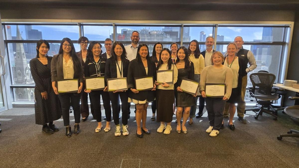 A group of people standing together, those in the front holding diplomas