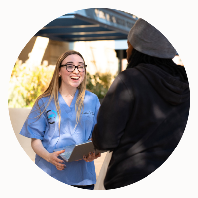 A person in hospital scrubs with a laptop, smiling at someone