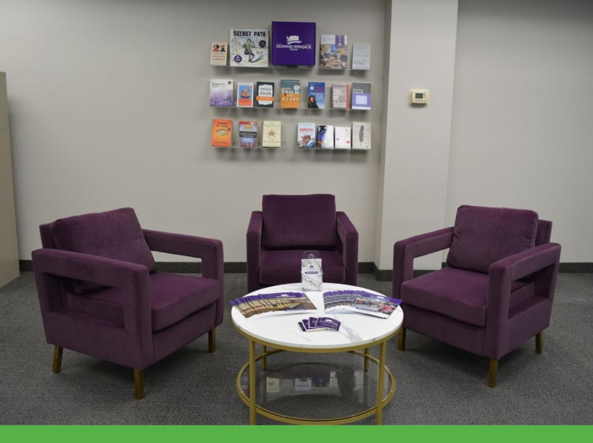 Three empty chairs, a table with pamphlets, and a collection of pamphlets on a wall in the background