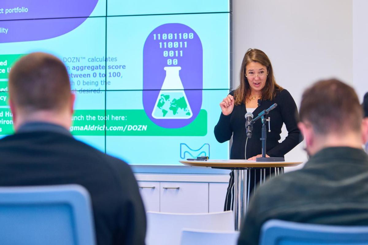 Woman standing at podium presents on "Green Chemistry" to an audience. 