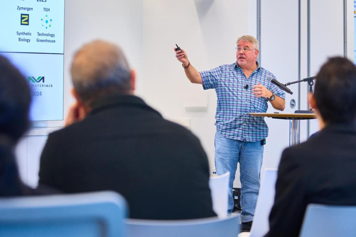 Man on stage points at presentation on "Green Chemistry" to an audience. 