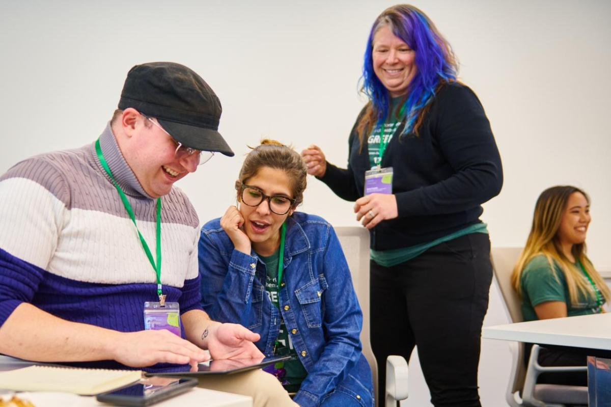 Three adults smiling while looking at a tablet.