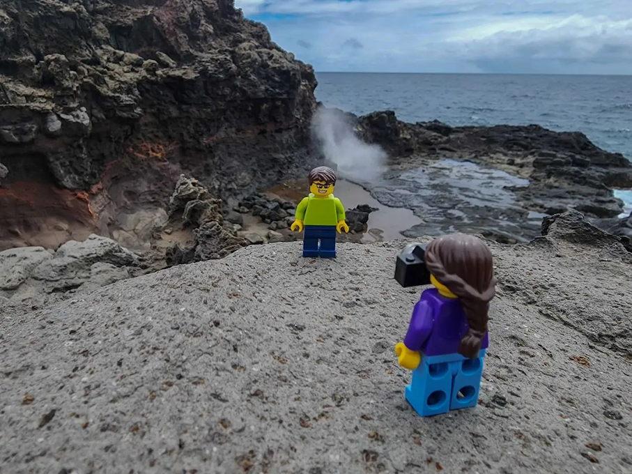 Two LEGO characters shown on a rock on a beach.