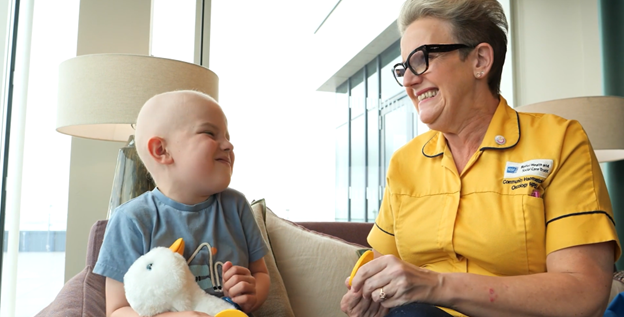 Young cancer patient holding the Aflac Duck and seated with a health professional.