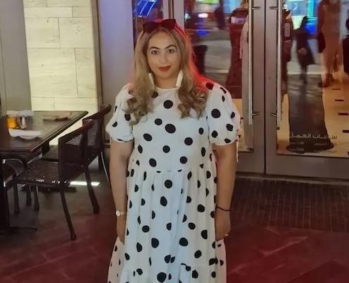 Aisha shown at a dinner in a white polka dot dress.