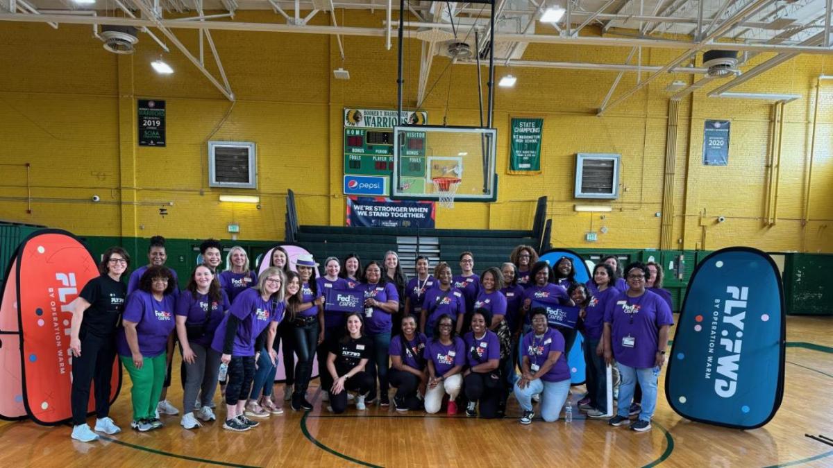 Female athletes wearing FedEx shirts standing together in gym