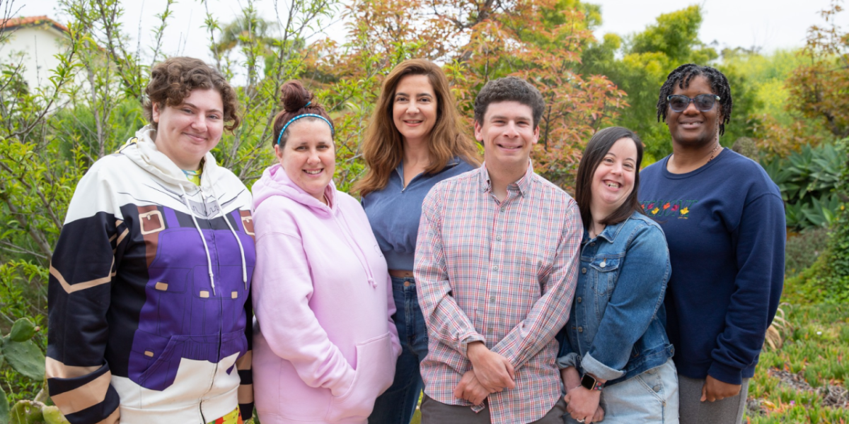 A group of people stood together smiling in front of some outdoor plants