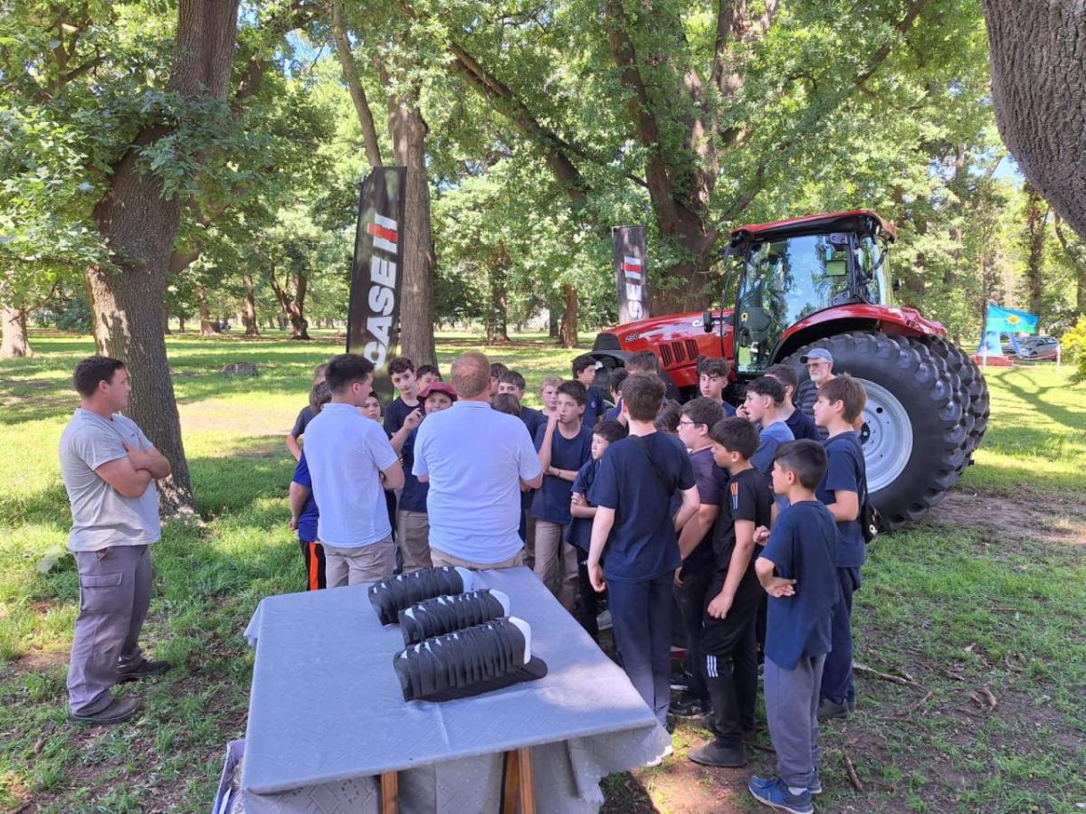 Two adults speaking to a group of students with a tractor behind them