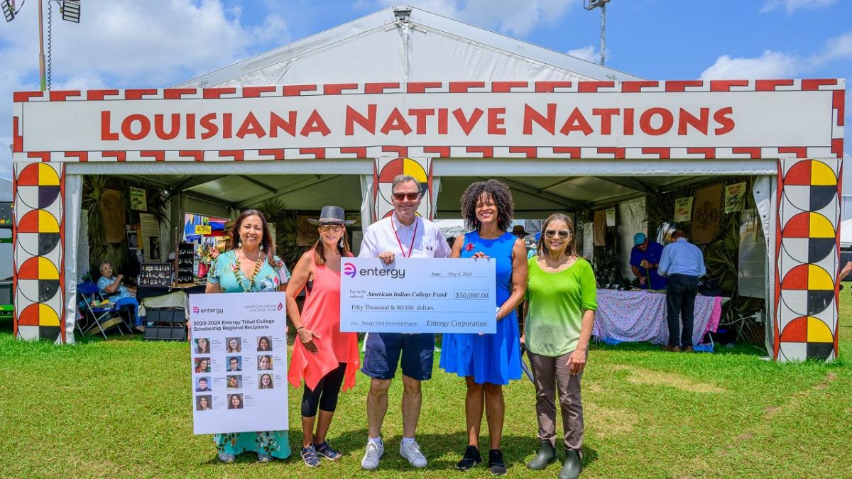 Five people posed with a large check and profiles of scholarship winners posed outside a booth "Louisiana Native Nations."
