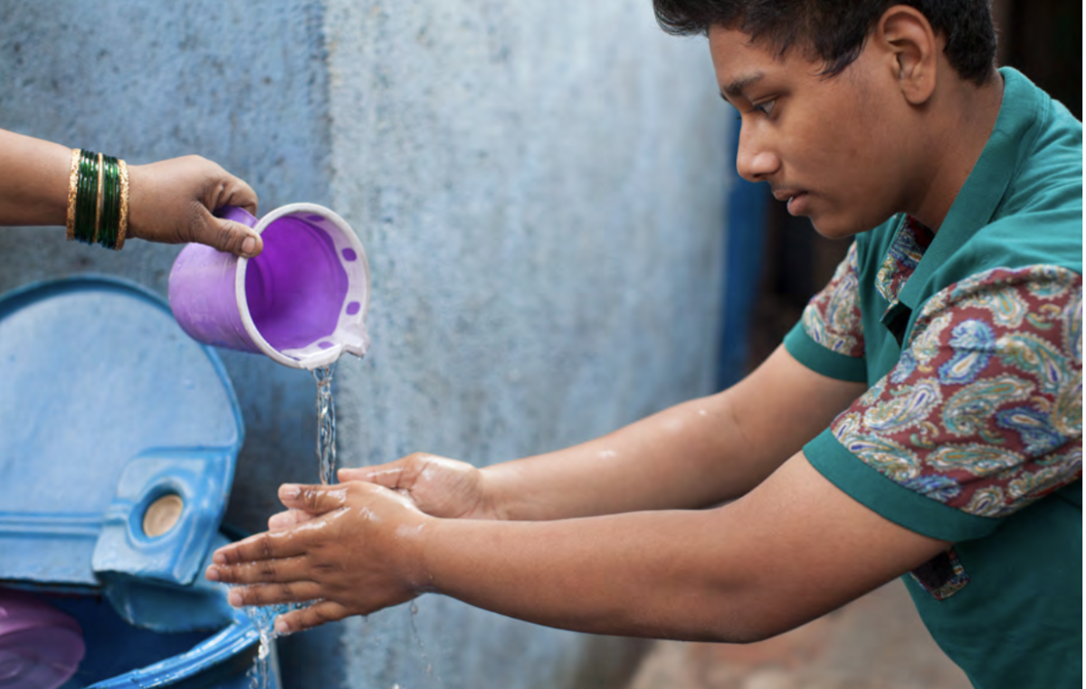 Young person having water poured over his hands so that they can wash them.