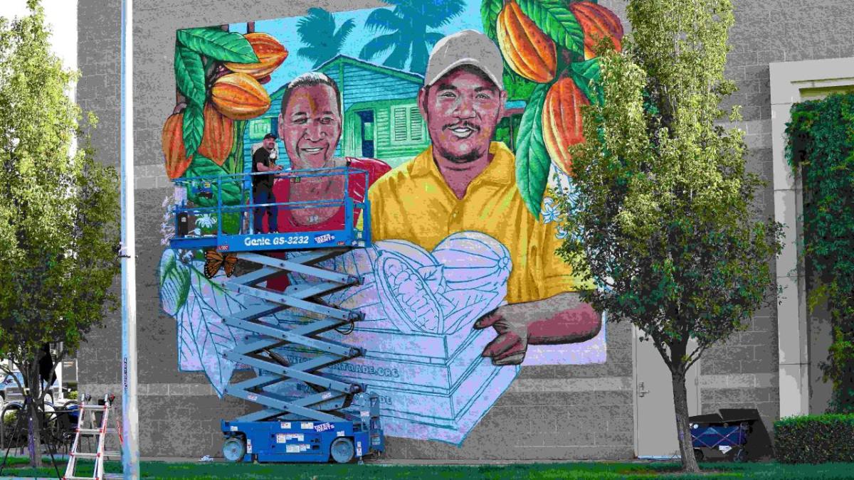 Artist Bobby Gaytan paints a mural of Francisco and Carlixta Martinez Contreras, sibling cocoa farmers from the Dominican Republic, outside Boise Co-op Market in Boise, ID.