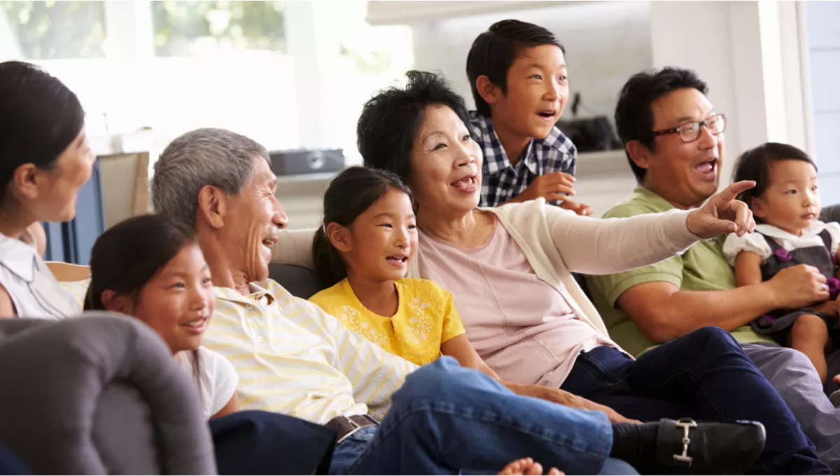 Asian family seated on a couch watching television.