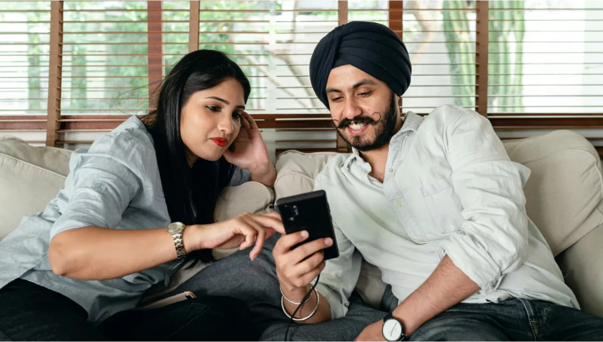 A couple seated on a couch looking at a smart phone. 