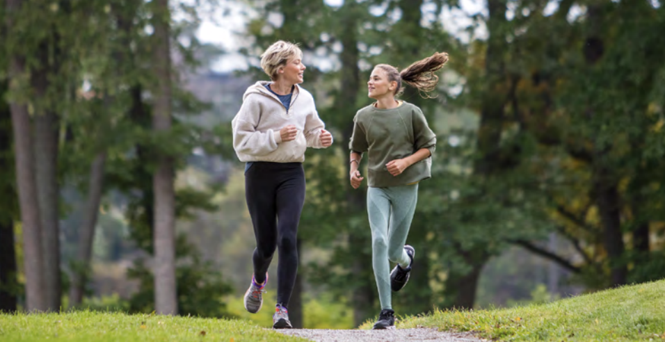 Two women jogging on a path on the edge of a forest.