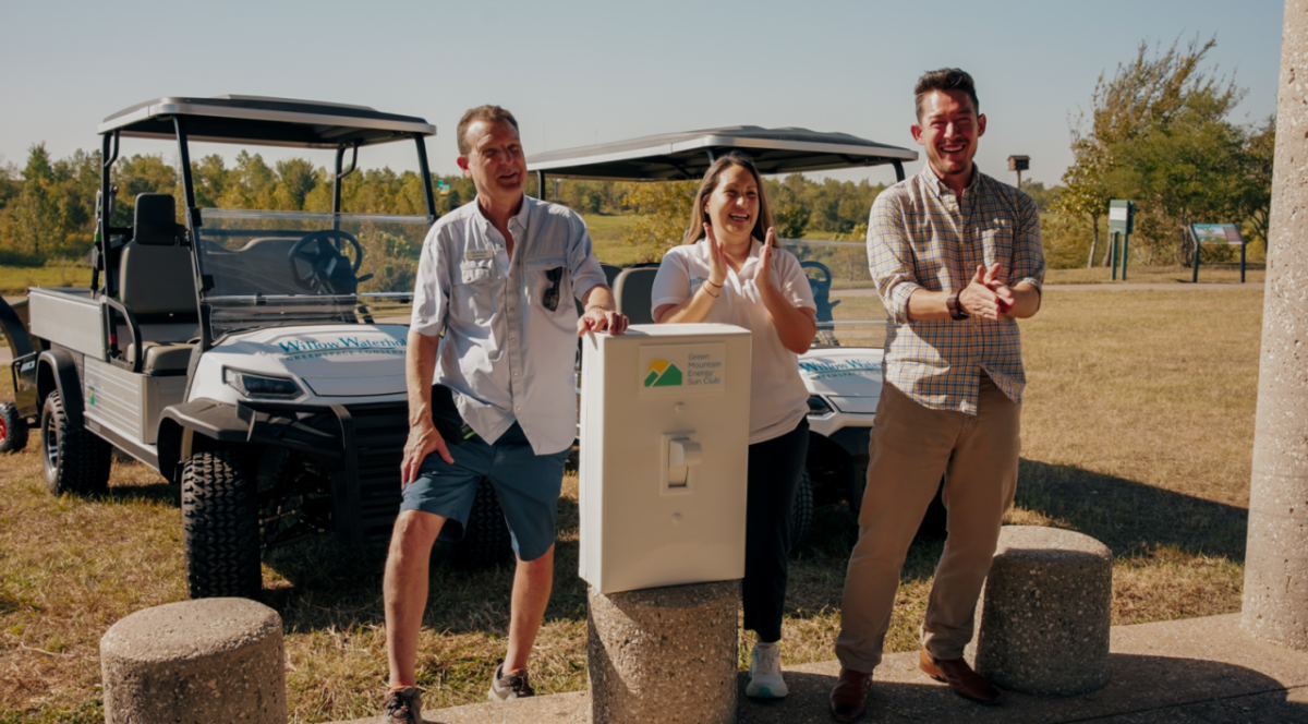 Two men and a woman stand smiling and clapping in front of two UTVs.