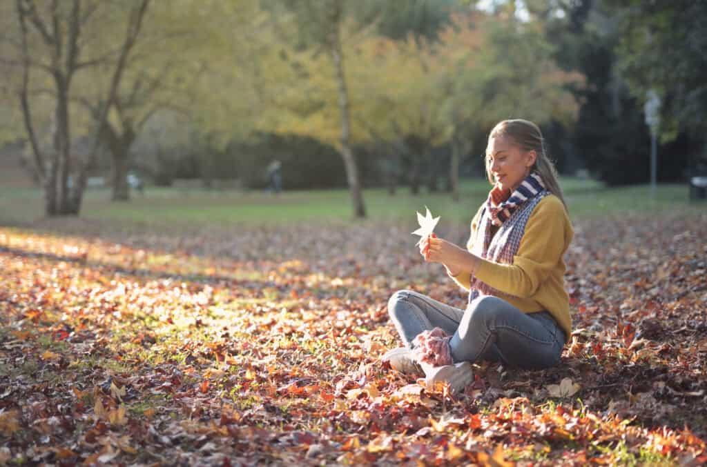 Image by Freepik* Young woman seated in a park in the fall holding a leave.