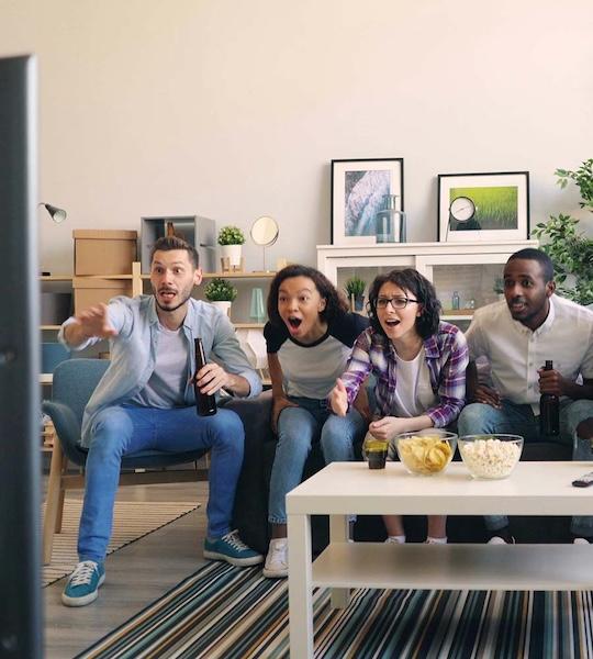 Four people watching tv while seated on a couch.