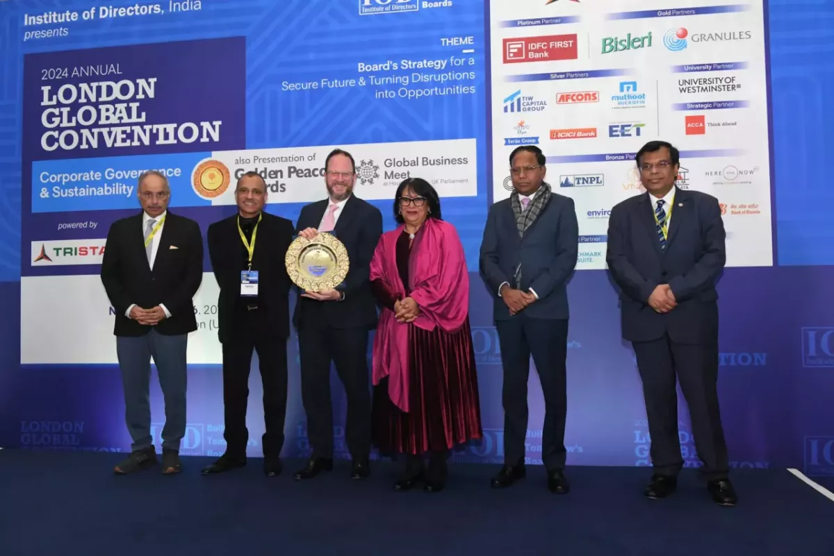 Six people posed in front of a large display "London Global Convention" One holds a golden award.