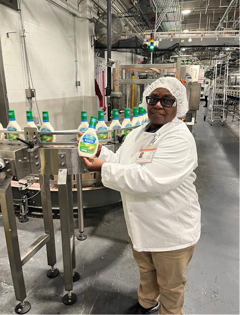 An employee hold up a bottle of ranch dressing in a manufacturing warehouse.