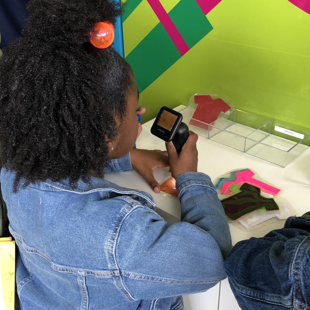 One student uses a microscope to examine the fibers of t-shirts through an interactive experiment.