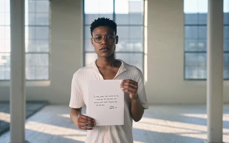 A person standing in a white room holding a sheet of paper.