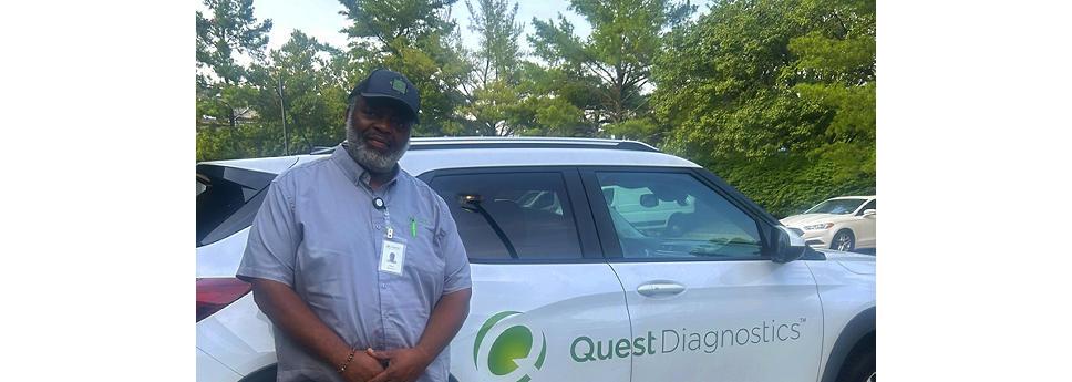 A person leaning against a white car that has the Quest Diagnostics logo on the side