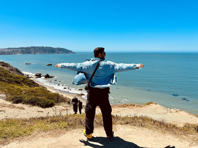 Jai Sharma shown on a beach with outstretched arms.