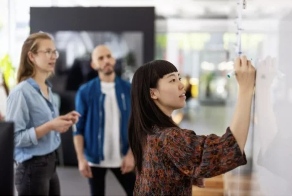 A woman making a presentation on a white board for two other people.