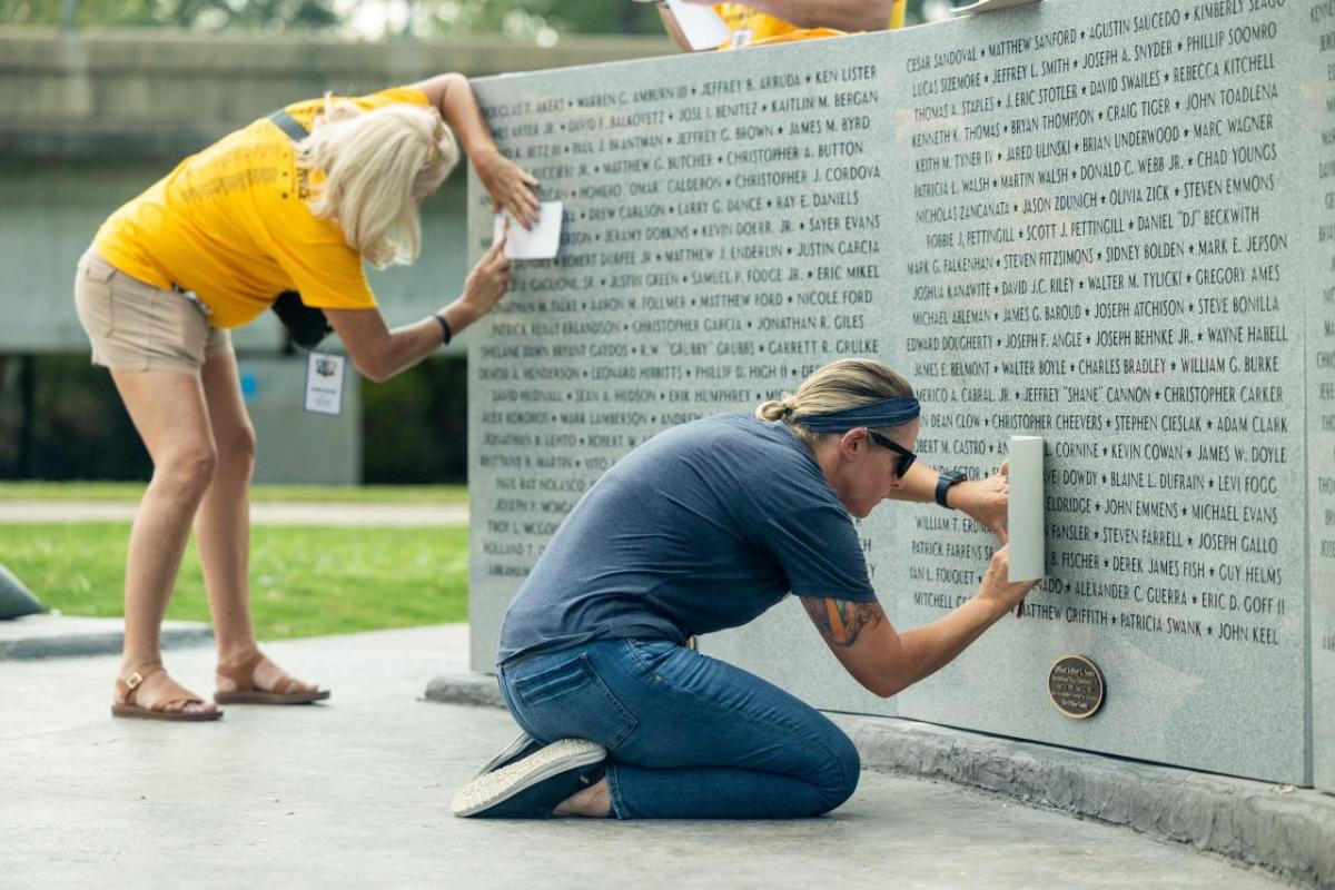 People tracing over names on the Heroes Memorial Park Monument