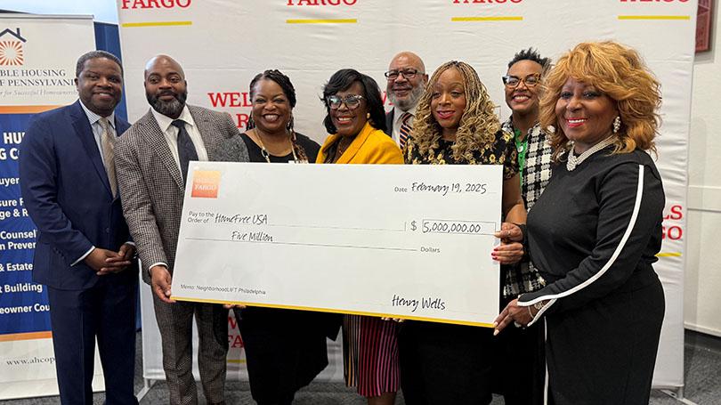 Group of people standing in front of a conference room holding a $5 million check.