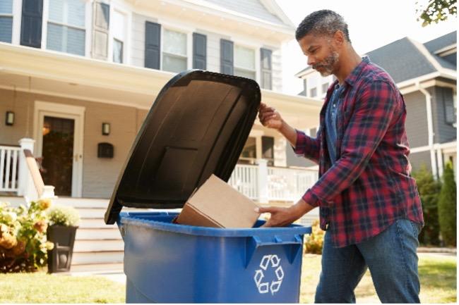 person putting box in recycling bin