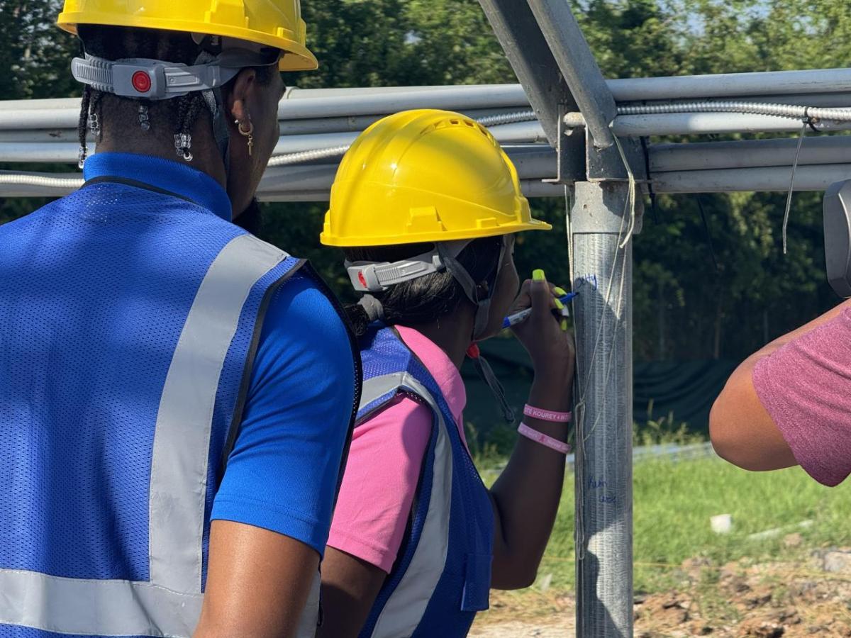 Girl in construction vest and hard hat signs greenhouse post with permanent marker.