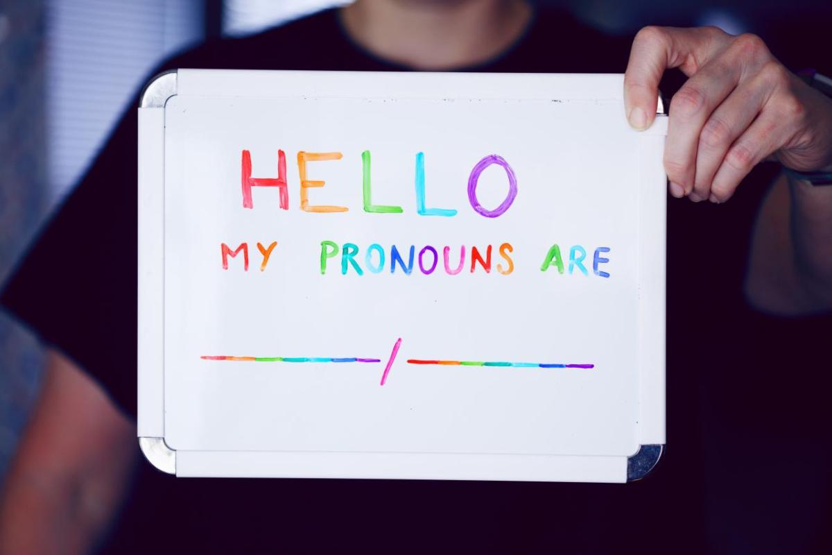 A person holding a sign with rainbow letters "Hello my pronouns are _/_"