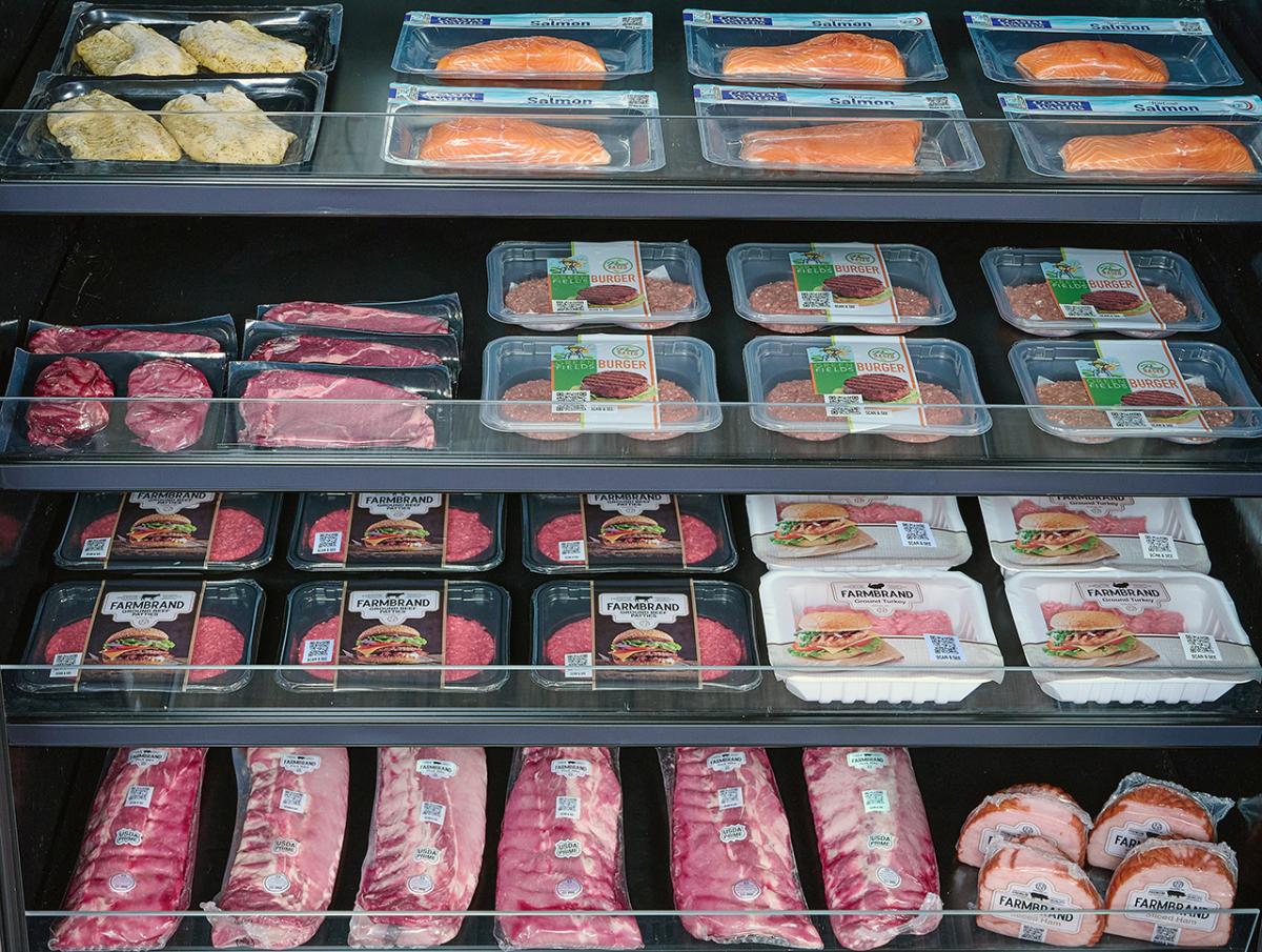 Packages of various proteins including meat and fish sitting on shelves in a refrigerated grocery store case