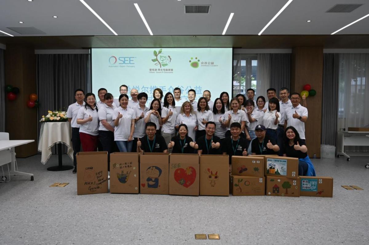 A large group of people stood together behind cardboard boxes 