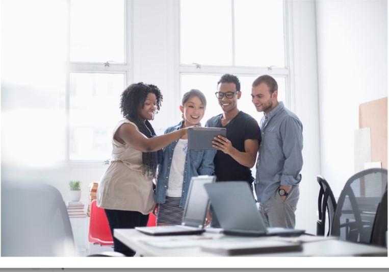 Two men and two women are sharing a tablet in a meeting room. 