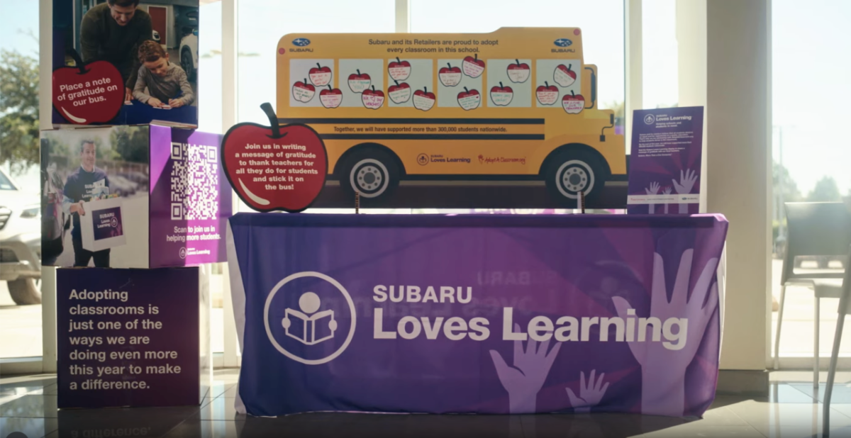 Still from a video showing a table with a paper school bus and signs about Subaru Loves Learning initiative