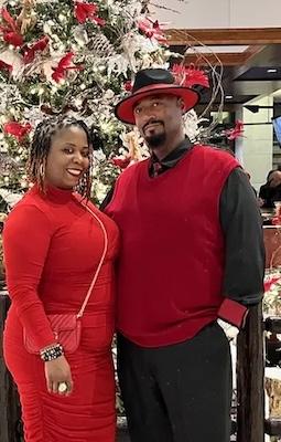 Trish and her husband dressed up and in front of a Christmas tree.