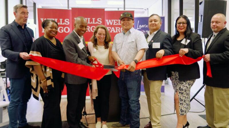 Group of people standing inside a brank branch cutting a red ribbon