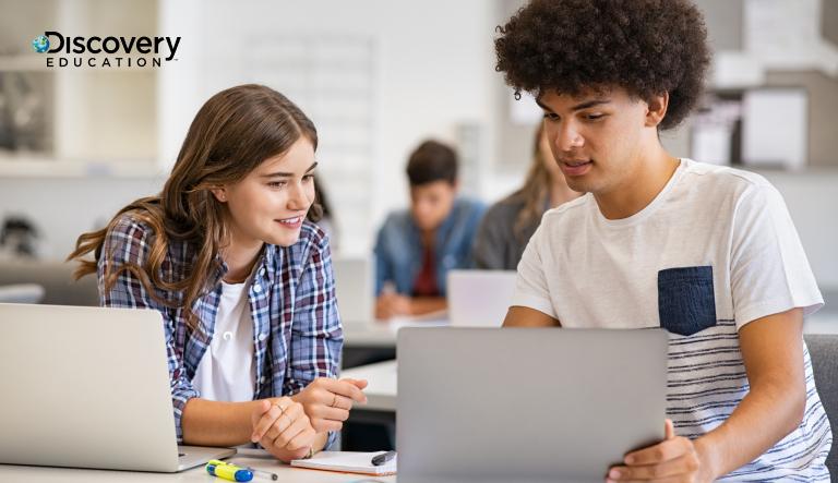 Two students looking at a laptop screen in a classroom