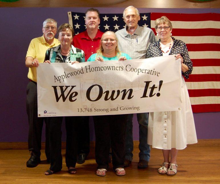Applewood Homeowners Cooperative group shown in front of an American Flag and holding a sign that says "We Own It".