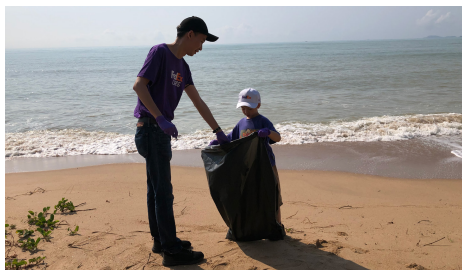 An adult and child holding a plastic bag on a beach.