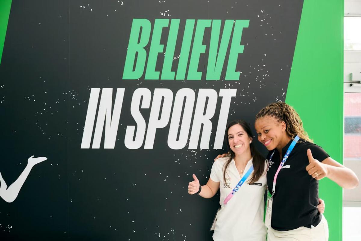 two people posing in front of "Believe in sport" banner