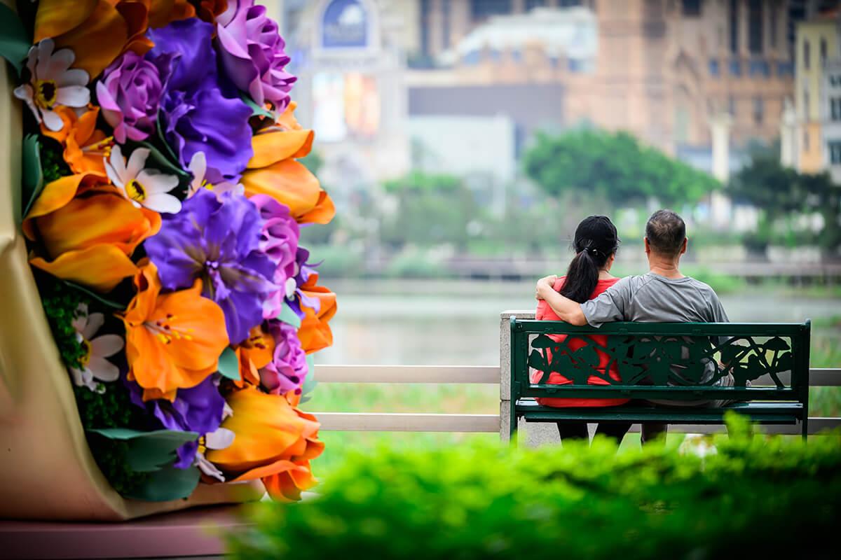 2 people sitting on a bench in front of flowers