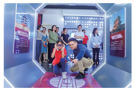 An adult and child crouched in an octagonal room with displays on each side. Others standing and waiting behind them.