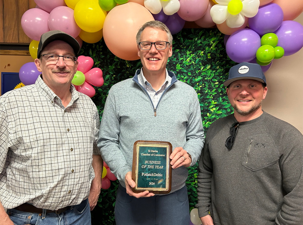 Three smiling people posed with a plaque. Balloons behind them.