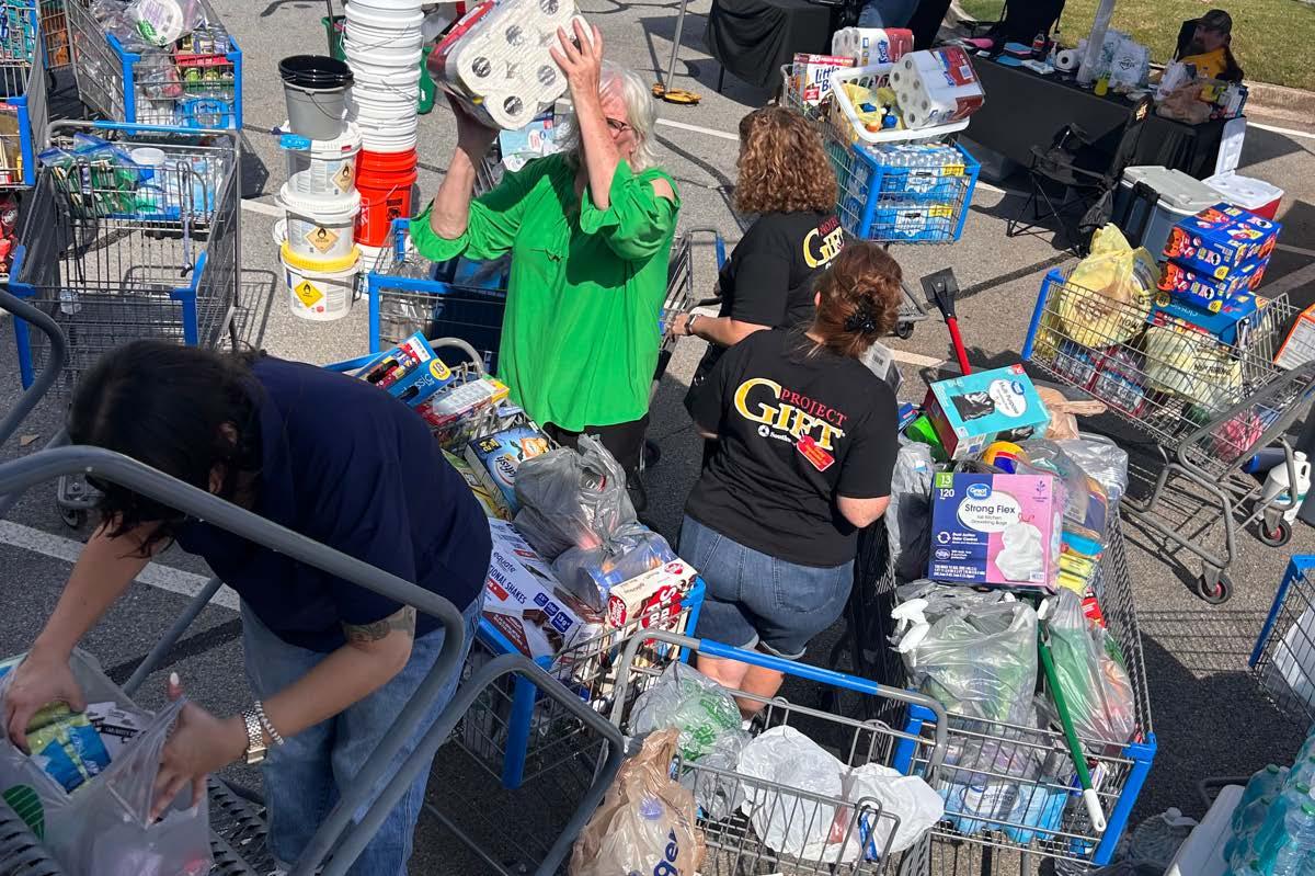 People sorting items into different grocery carts in a parking lot.